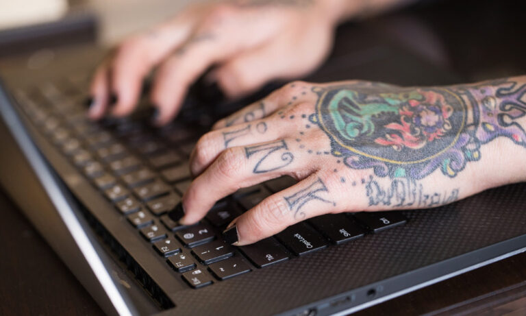 Tattooed hands typing on a laptop