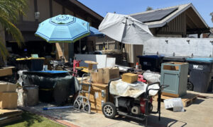Front yard and driveway of a Mission Viejo home with boxes, storage bins, appliances, and other items scattered around the property